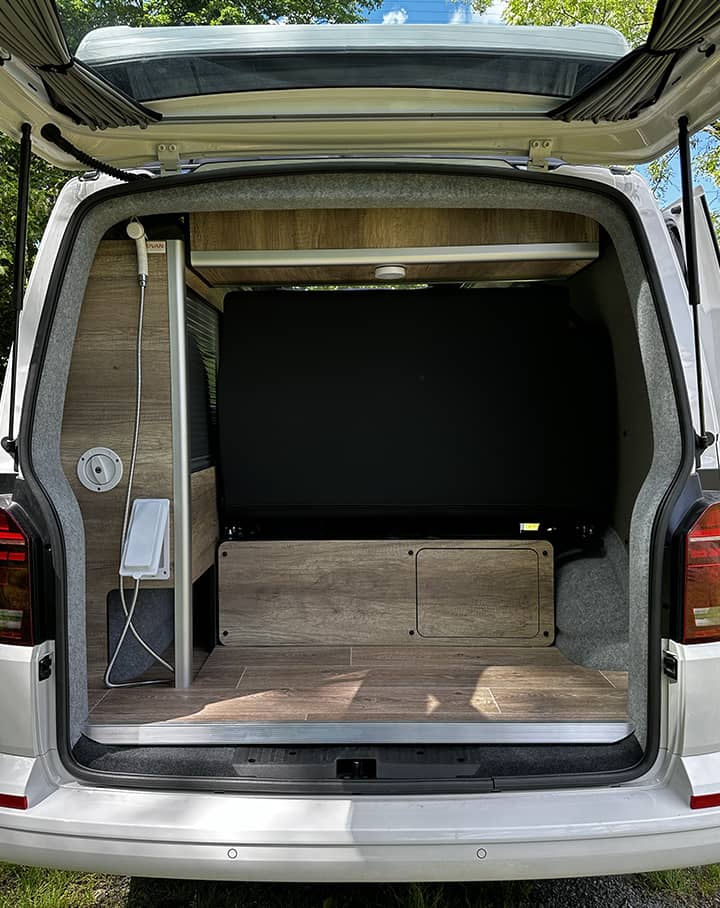 Vue arrière d’un van aménagé avec le pack eau chaude, équipé de rangements en bois et d’un espace optimisé pour les escapades en pleine nature