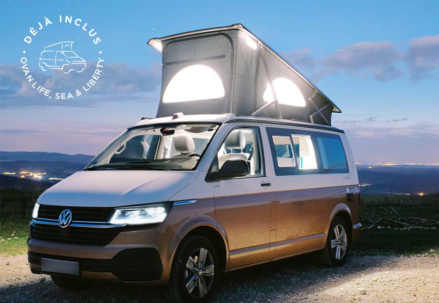 Van Volkswagen avec toit relevable éclairé, en extérieur de nuit, avec vue sur un paysage lumineux.