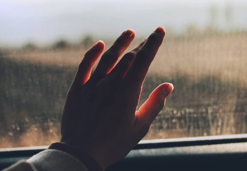 Une main touchant une vitre embuée d’un van, avec une vue floutée sur l’extérieur