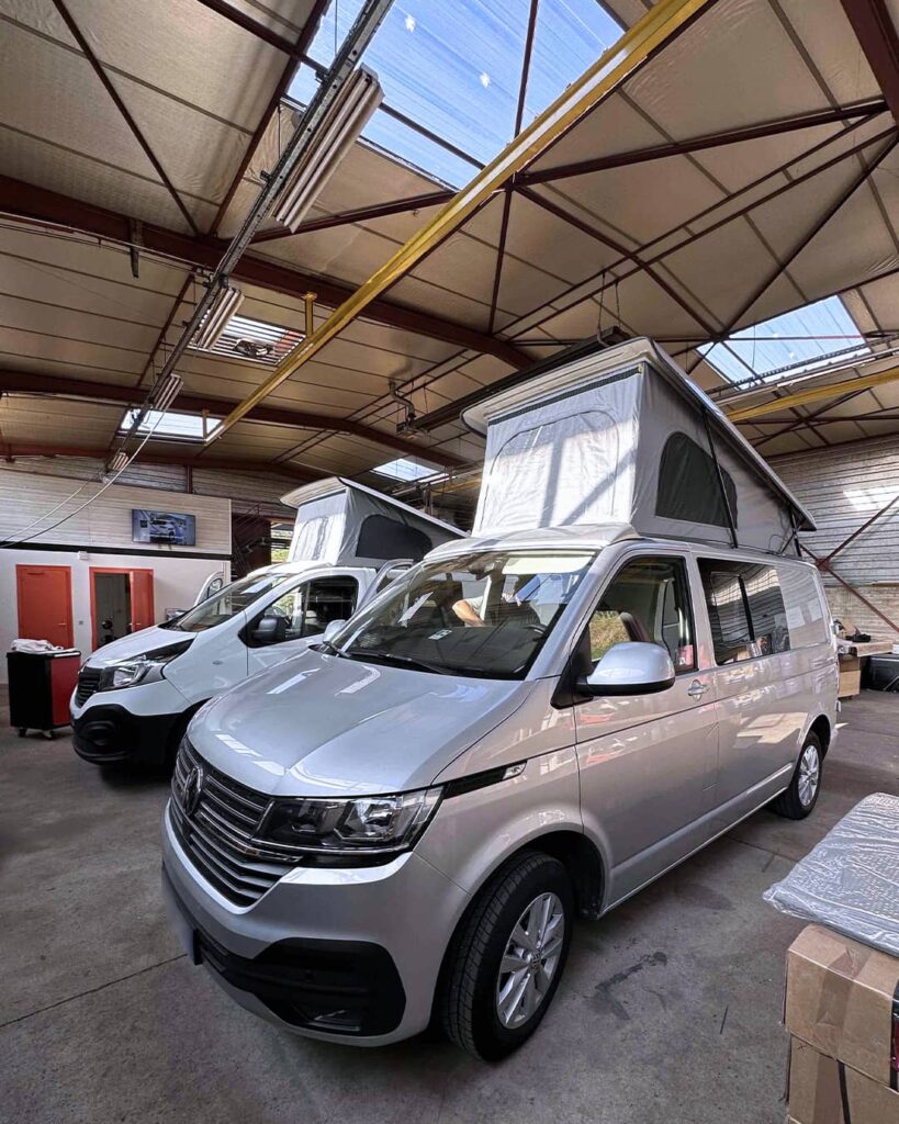 Vans aménagés avec toits relevables en cours d'installation dans un atelier professionnel.