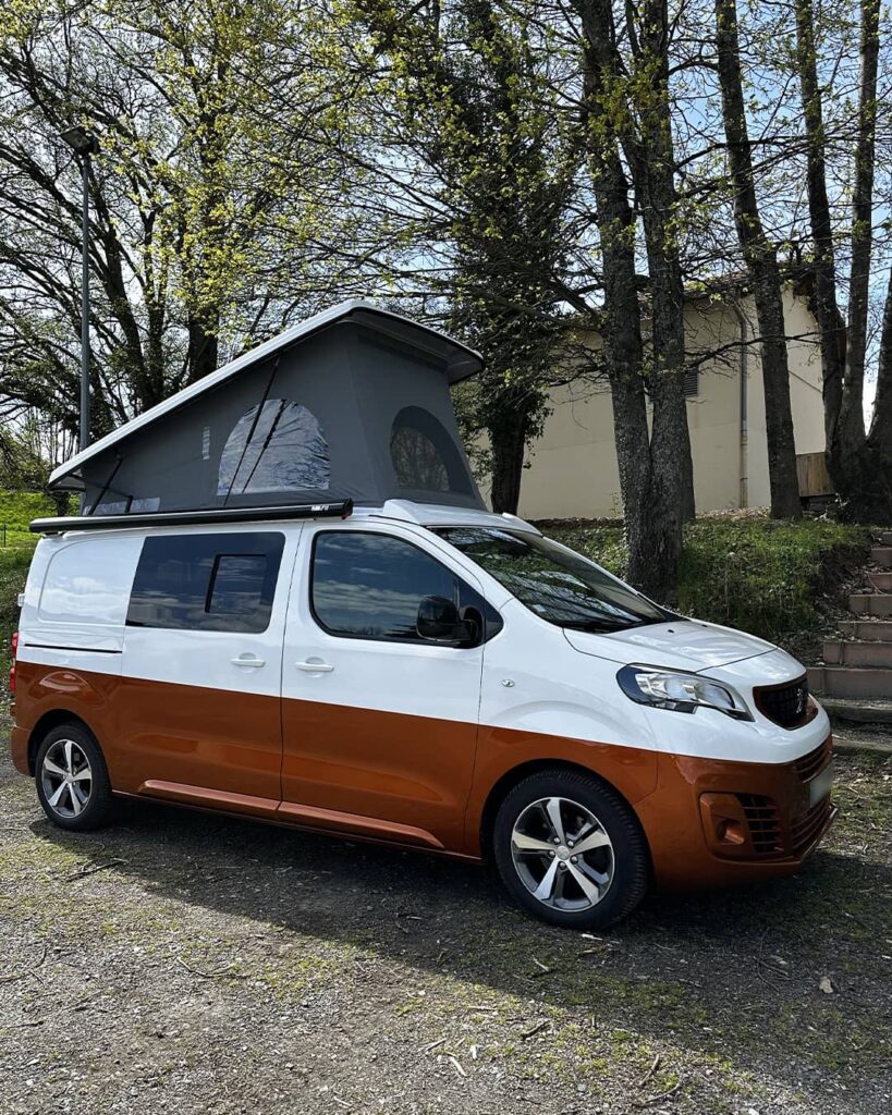 Van aménagé bicolore blanc et orange avec un toit relevable déployé, stationné en extérieur