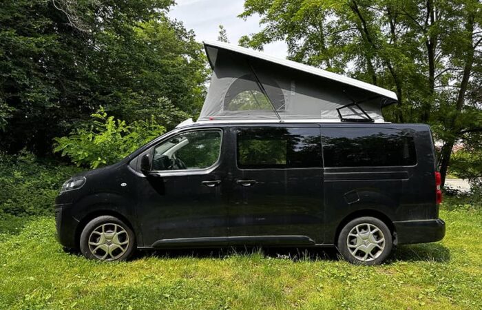 Van aménagé noir avec toit relevable SCA 264 ouvert, en pleine nature