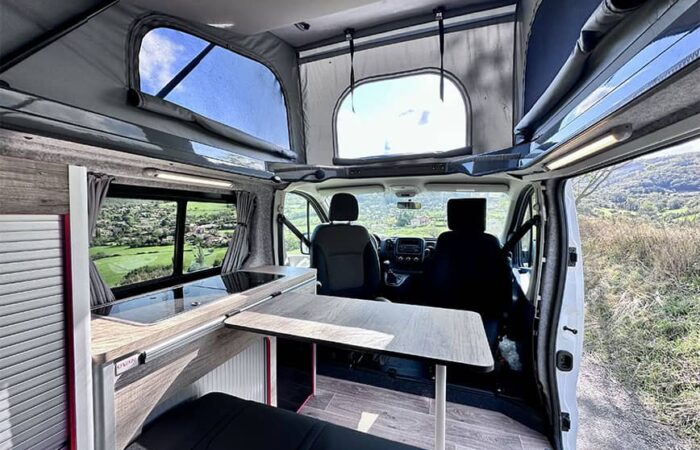 Intérieur d'un van aménagé Ovan avec toit relevable, table pliable et vue panoramique sur la campagne