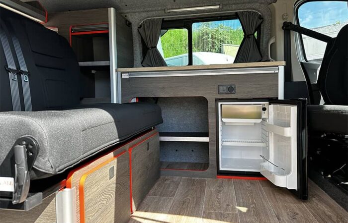 Aménagement intérieur d'un van Ovan avec banquette convertible, réfrigérateur intégré et espace de rangement