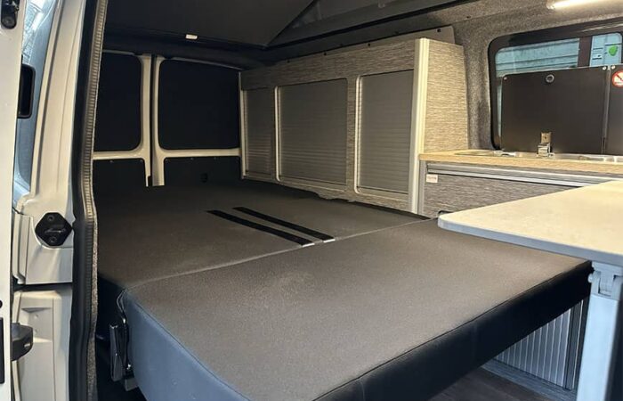 Banquette dépliée en lit dans un van aménagé par Ovan avec rangements et table intégrée