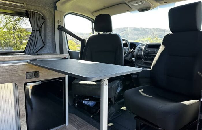 Intérieur d'un van aménagé par Ovan avec table modulable, sièges pivotants et réfrigérateur intégré