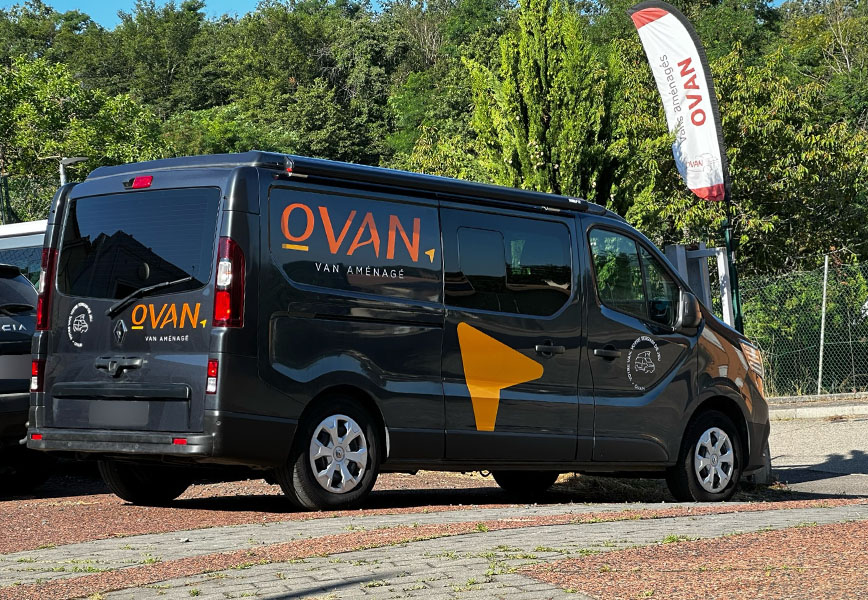 Van aménagé Ovan, modèle Renault Trafic noir, garé devant le showroom, arborant le logo Ovan et des éléments graphiques.