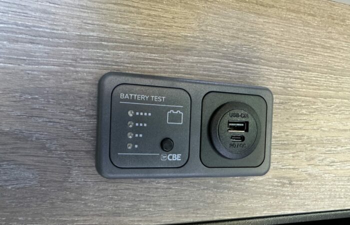 Gros plan d'un panneau de test de batterie CBE avec indicateurs LED et un port de charge USB-C/A monté sur une surface texturée en bois.